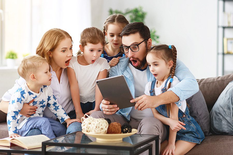 Client Center - Parents and Four Young Kids Together on Sofa Looking at a Tablet in Amazement