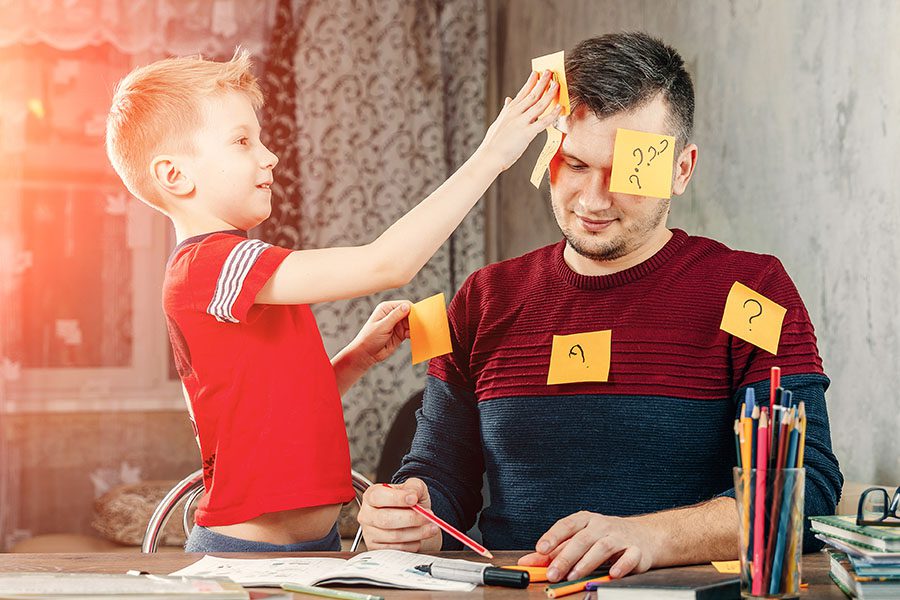 Personal Insurance - Father and Son Sitting at a Table Having Fun Together While the Son Sticks Post It Notes on His Father